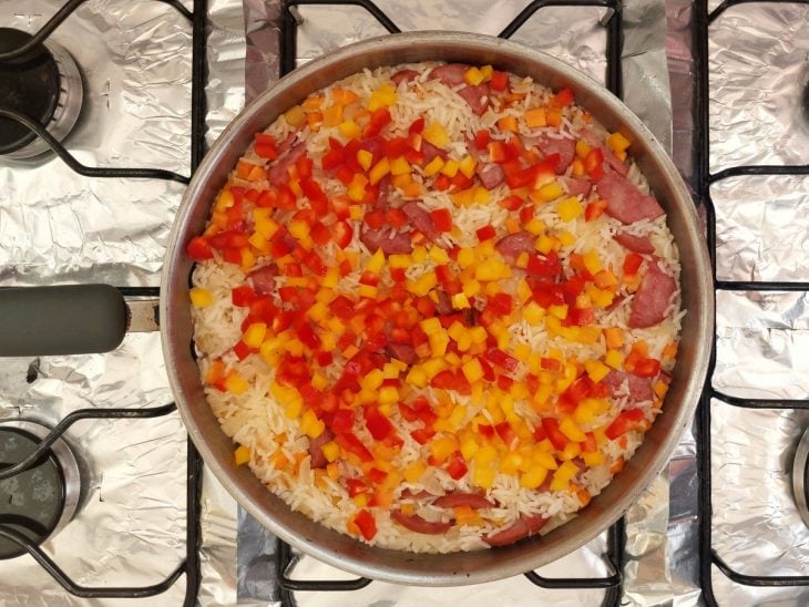 Uma panela refogando calabresa, cebolas, legumes e arroz.