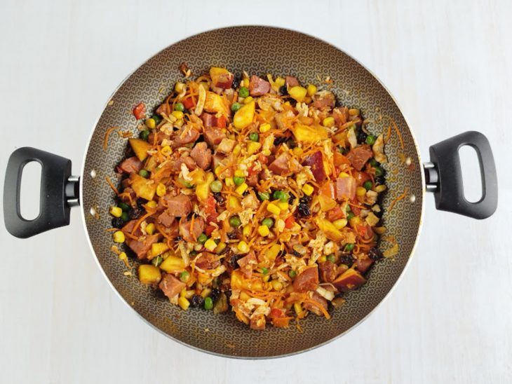 Na panela, o frango, a cenoura, o milho, a ervilha, a maçã e as uvas passas adicionadas.