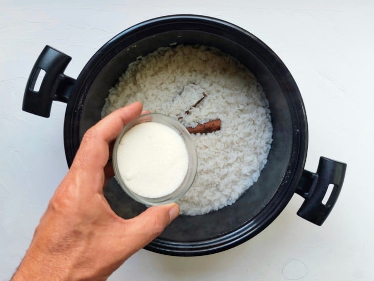 Uma panela com arroz, água fervendo, paus de canela e açúcar.