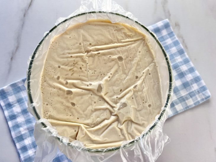 Um recipiente contendo arroz doce com leite condensado coberto com plástico filme.