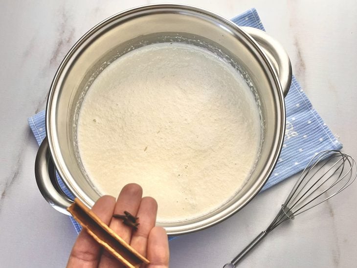 Uma panela com leite em pó, água, coco ralado, arroz, cravos-da-índia e canela.