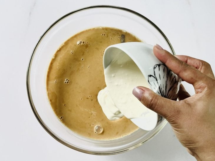 Tigela de vidro com o creme de leite sendo adicionado ao arroz-doce.