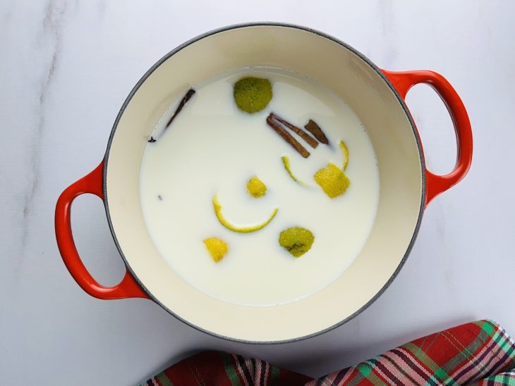Uma panela com leite, canela em pau, cravos e casca de laranja.