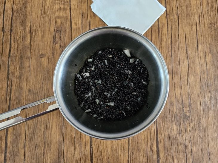 Arroz negro adicionado na panela com temperos.