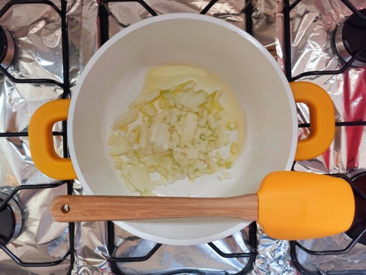 Azeite e cebola cortada em uma panela em cima do fogão.