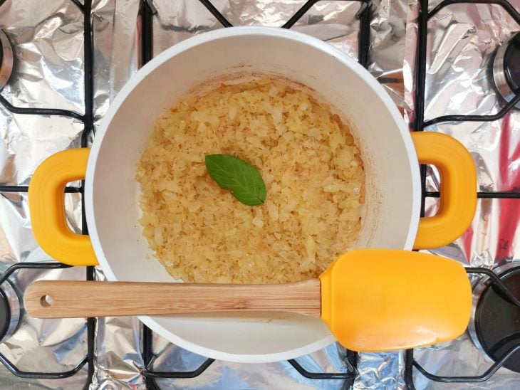 Arroz e folha de louro adicionados na panela com cebola e azeite.