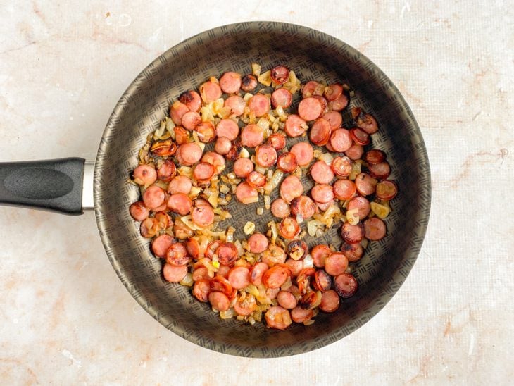 Linguiça, cebola e alho fritos em uma frigideira.