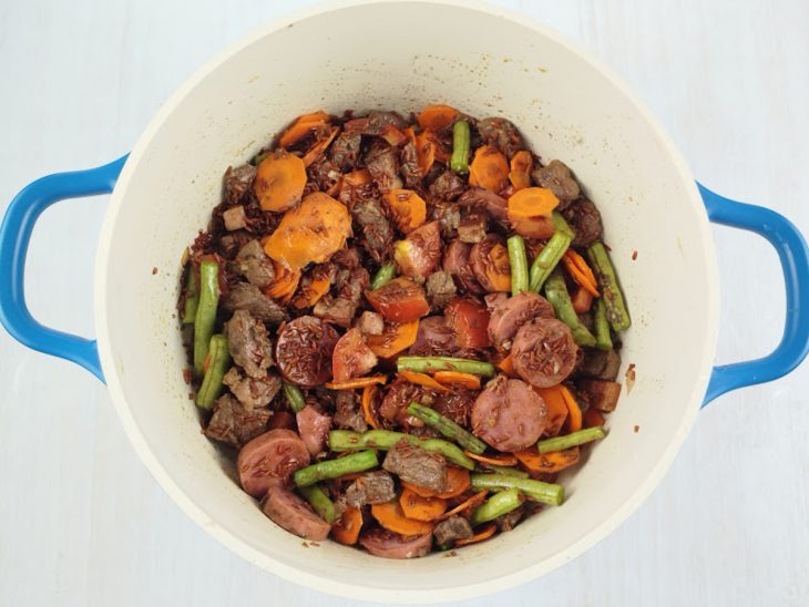 Cenoura, vagem e tomate adicionados na panela, junto com caldo de carne e temperos.