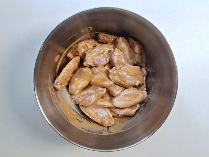 Asinhas de frango adicionadas a tigela com a mistura.