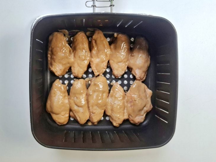 Asinhas temperadas posicionadas no cesto da air fryer.