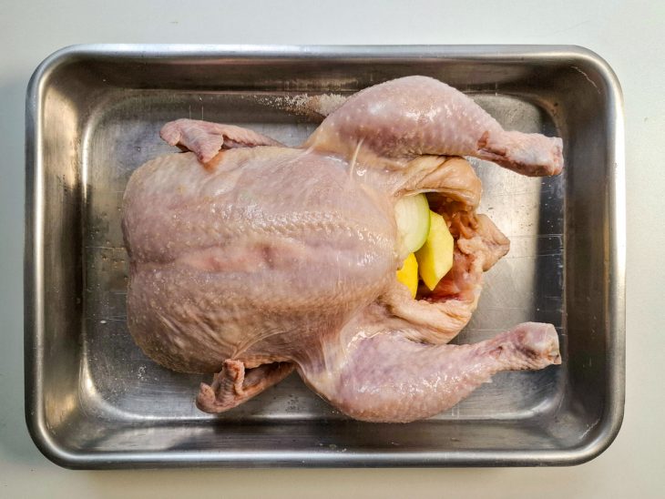 Numa assadeira, a ave coberta de sal e recheada com a maça e a cebola.