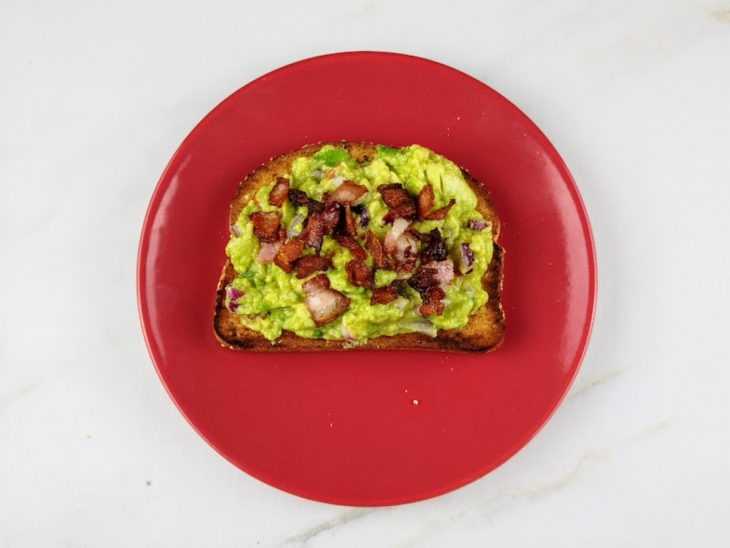 Mistura de avocado e bacon acomodados sobre a fatia de pão torrado.