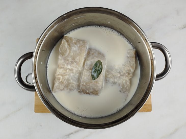 Uma panela com lombo de bacalhau, leite, folha de louro e alho.