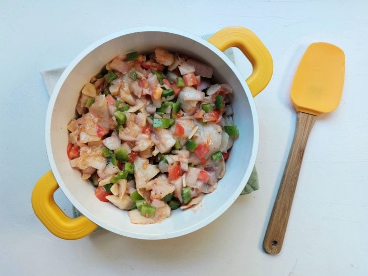 Uma panela contendo bacalhau dessalgado, alho, cebola, tomate, pimentão, molho de tomate e temperos.