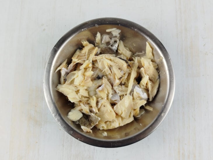 Bacalhau cozido sendo limpo e separado em pedaços maiores após a retirada dos espinhos.