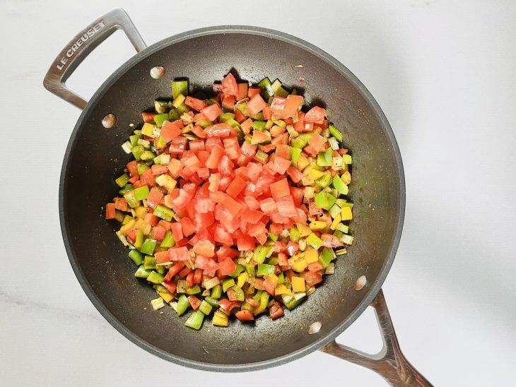 Uma frigideira com alho, cebola, pimentões, tomate e temperos refogando.