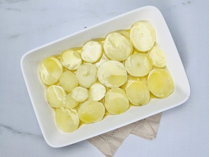 Um refratário com azeite e rodelas de batata.