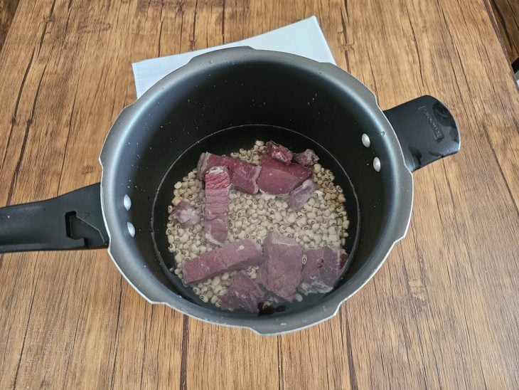 Uma panela de pressão contendo água, carne-seca e feijão.