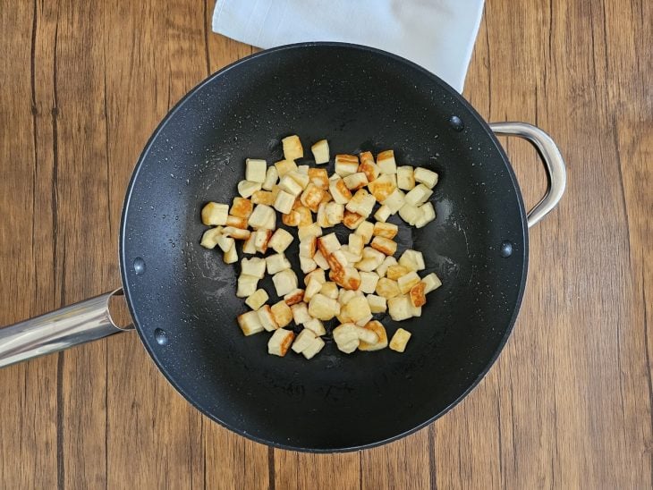 Uma frigideira contendo queijo em cubos douradinhos.