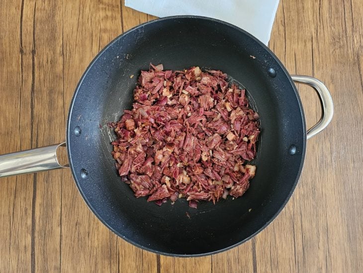 Uma frigideira contendo queijo e carne seca sendo refogados.