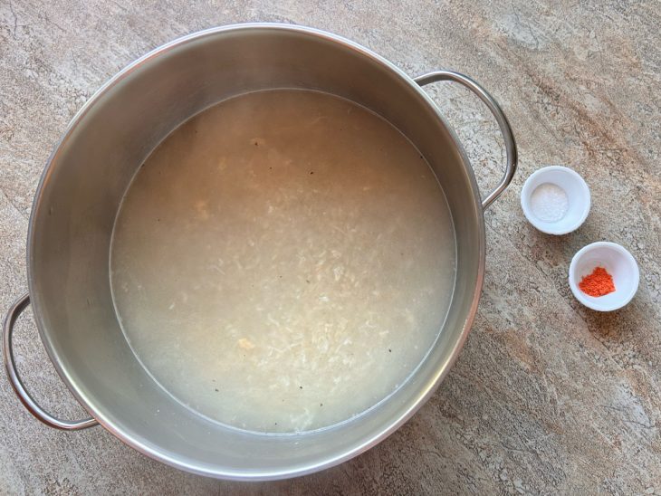 Arroz na panela submerso em água, ao lado, o sal e a páprica separados para serem adicionados.