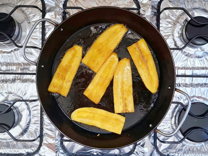 Fatias de banana fritando na frigideira com óleo.