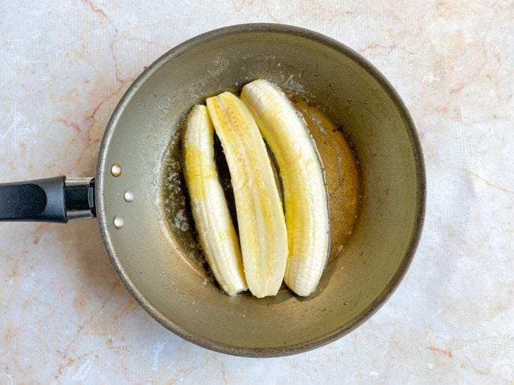 Fatias da banana colocadas na frigideira com manteiga derretida.