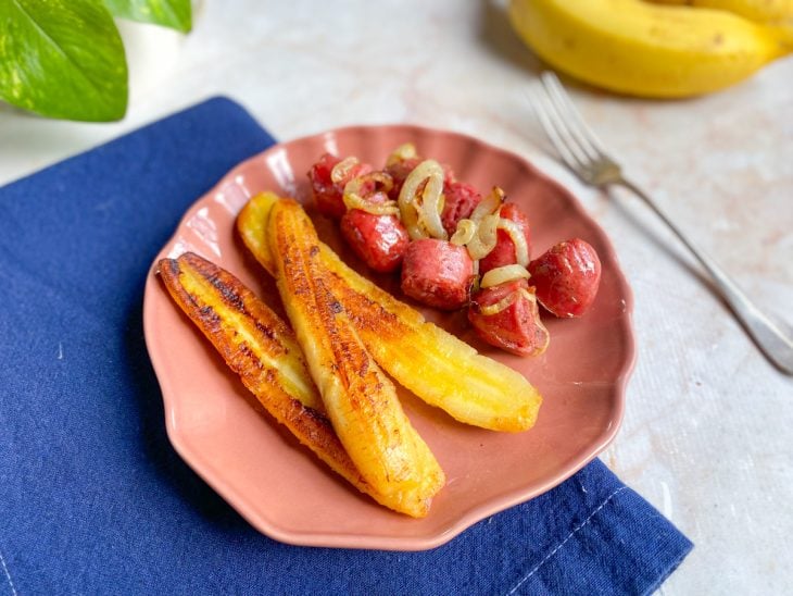 Banana-da-terra grelhada pronta para consumo e acompanhada por linguiça toscana acebolada.