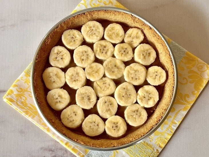 Uma forma com a massa coberta com doce de leite e rodelas de banana.