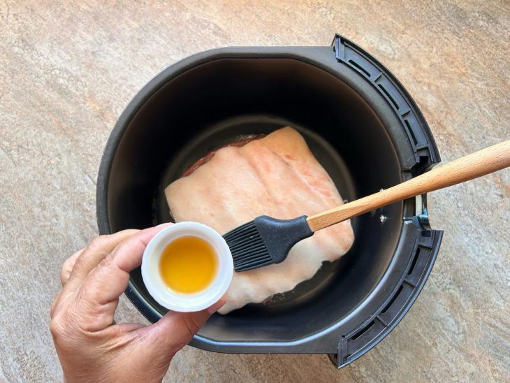 Peça da barriga no cesto na air fryer, sendo pincelada cm vinagre.
