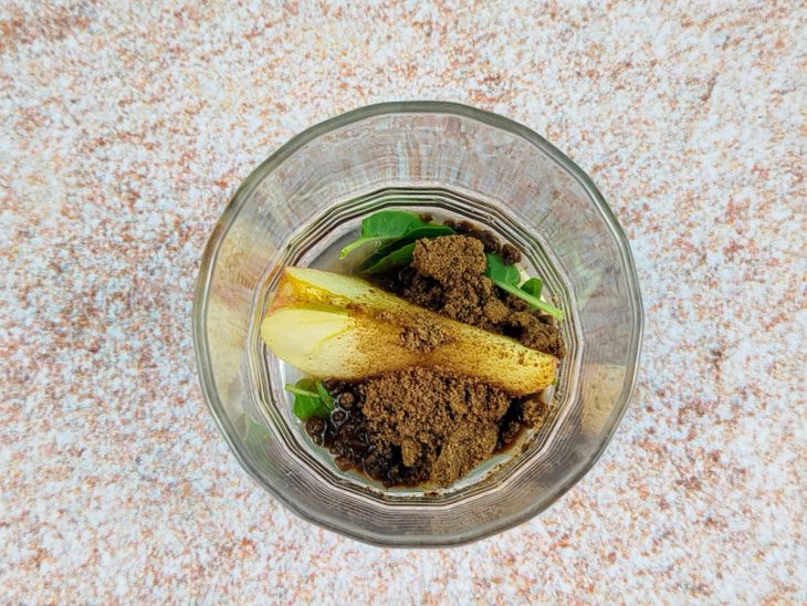 Copo com uma fatia de maçã, folhas de manjericão, açúcar mascavo e suco de limão.