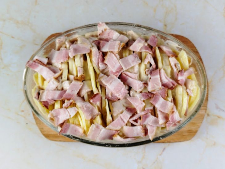 Camadas de creme, batata e bacon adicionadas em uma travessa de vidro.