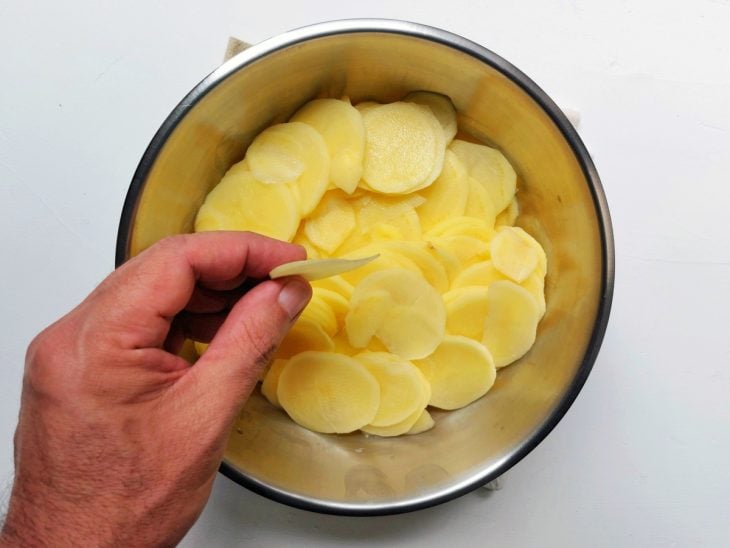 Um recipiente contendo batatas cortadas finamente em rodelas.