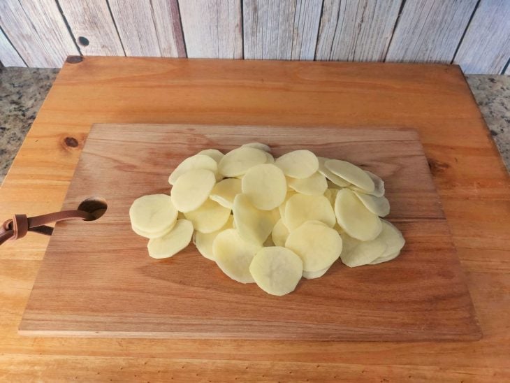 Uma tábua contendo batatas fatiadas finamente.