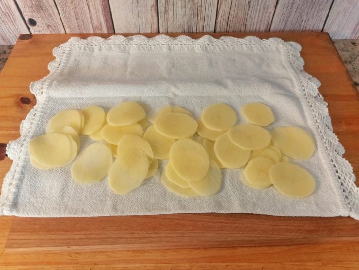 Uma bancada contendo um pano estendido com batatas fatiadas por cima.