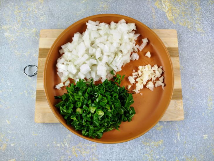 Cebola, cebolinha e salsinha picadas em um prato.