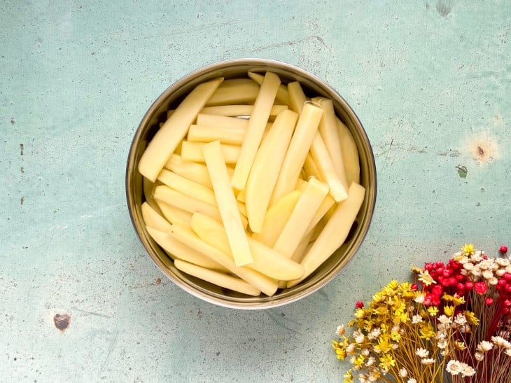 Um recipiente com batatas em palitos lavadas.