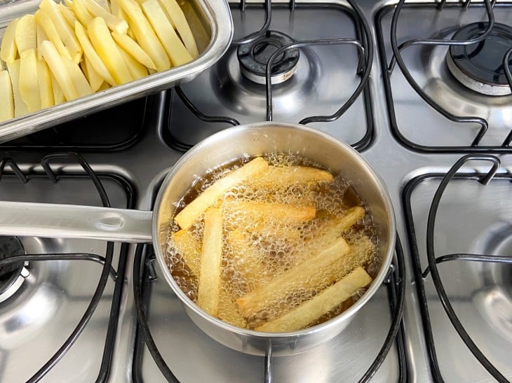 Uma frigideira com óleo fritando as batatas.