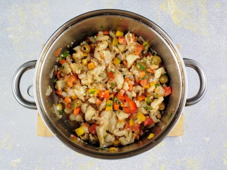Bacalhau, temperos e legumes refogando na panela.