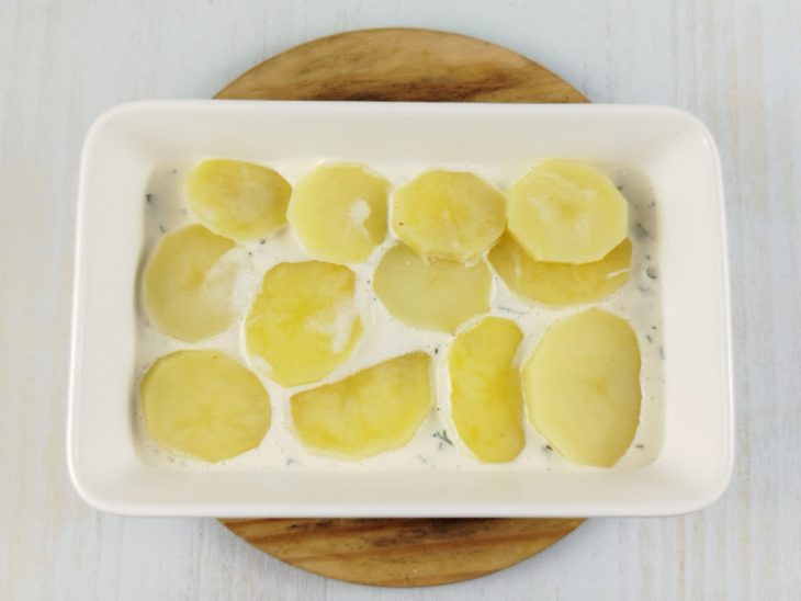 Num refratário, camada de molho sob as batatas.