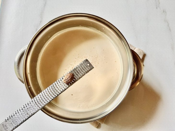 Manteiga, alho, farinha de trigo, creme de leite, leite, noz-moscada e sal em uma panela.