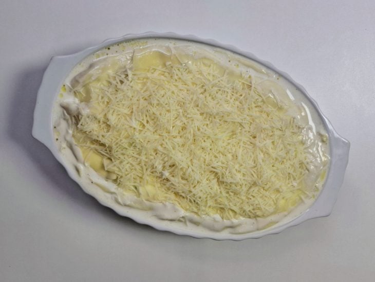 Um refratário com as batatas, o molho e o queijo por cima.