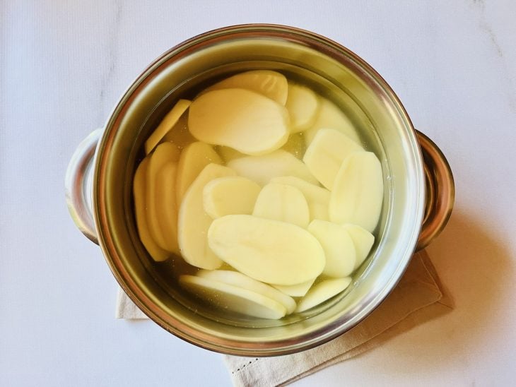 Rodelas de batatas em uma panela com sal e água.