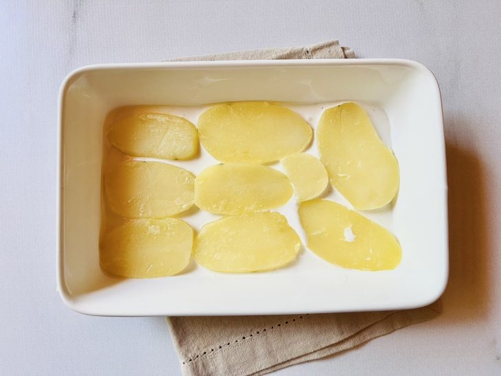 Travessa com uma camada de molho branco e uma de batatas.