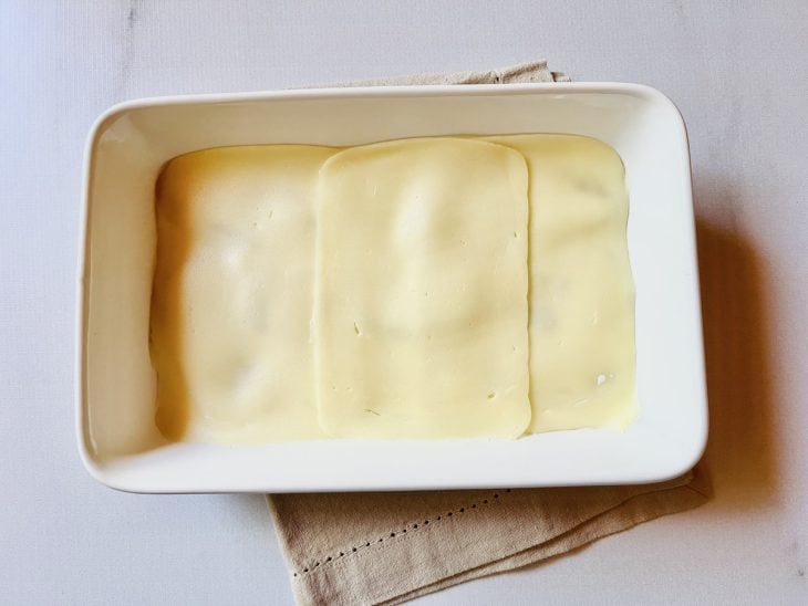 Camada de molho branco e queijo mussarela adicionados a travessa.