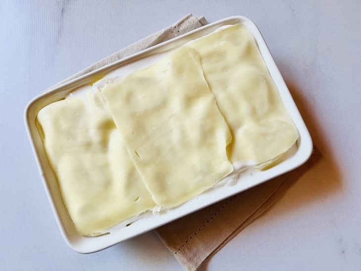 Travessa preenchida com camadas de molho, batata e queijo.