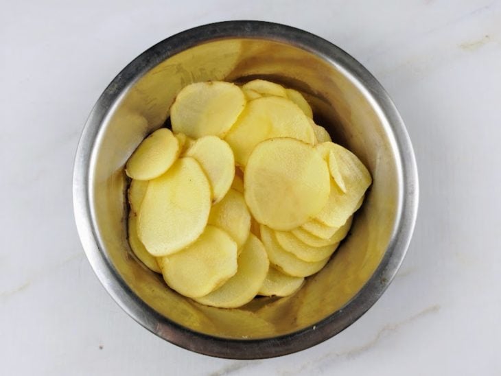 Batatas em rodelas dentro de um recipiente de alumínio.