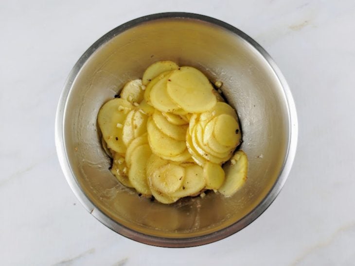 Azeite, sal, pimenta, noz-moscada e alho adicionados ao recipiente com as batatas.