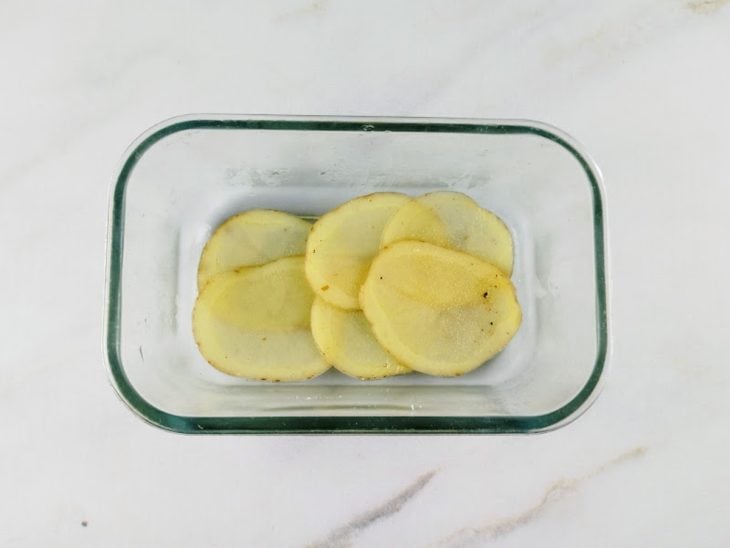 Refratário de vidro com uma camada de batatas em rodela ao fundo.