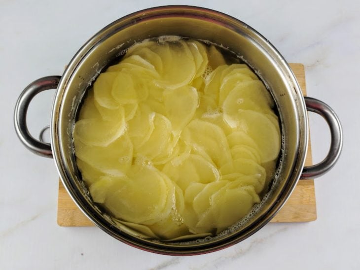 Rodelas de batatas cozinhando em uma panela com água.